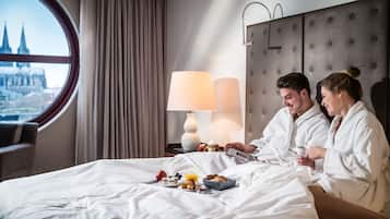 Habitación de hotel con una cama, una mesita de noche con lámpara y vista a un paisaje urbano a través de una ventana.