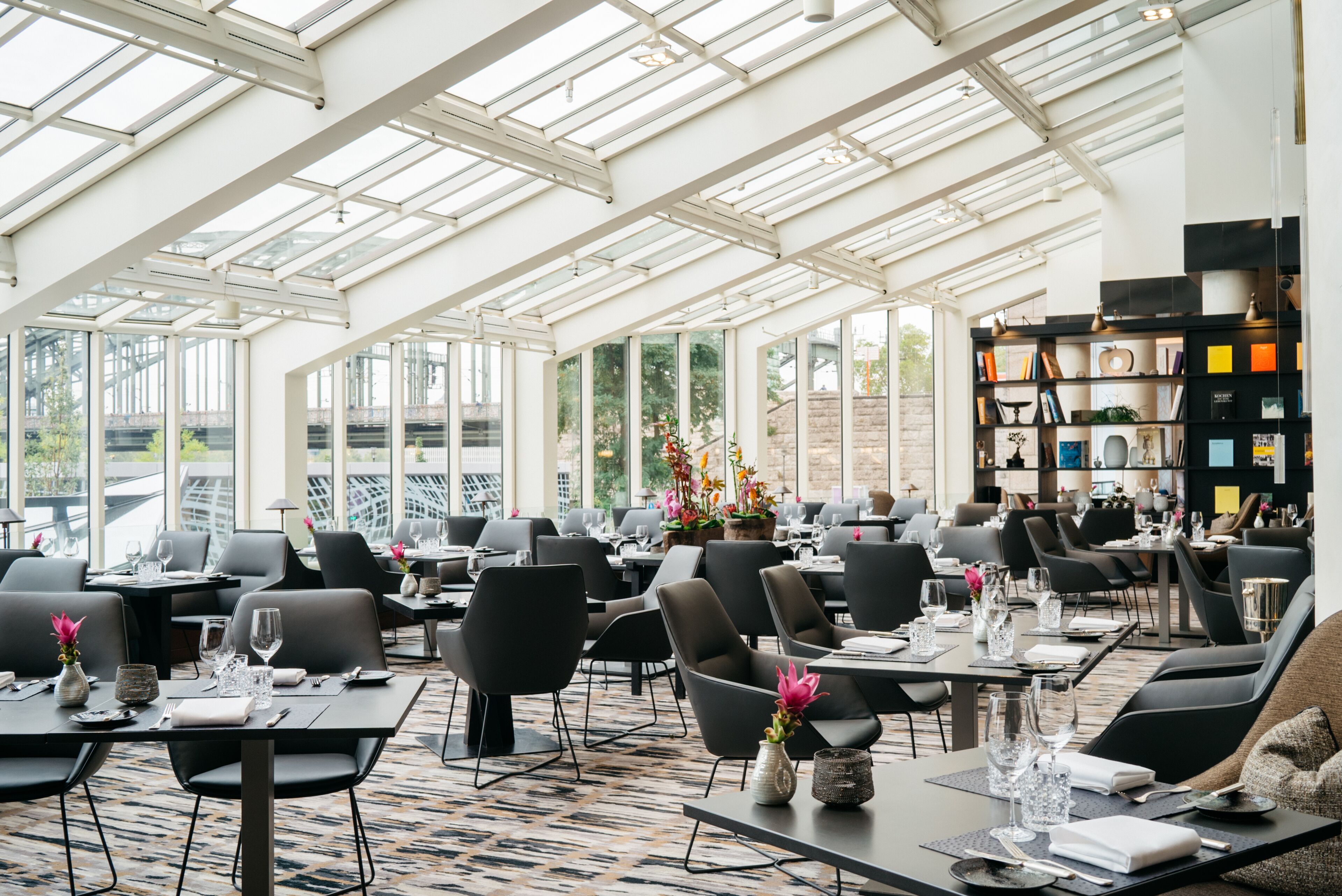 Ein großzügiges Restaurant mit hohen Decken und großen Fenstern, moderner Einrichtung und einer klaren Raumaufteilung.