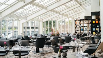 Ein großzügiges Restaurant mit hohen Decken und großen Fenstern, moderner Einrichtung und einer klaren Raumaufteilung.