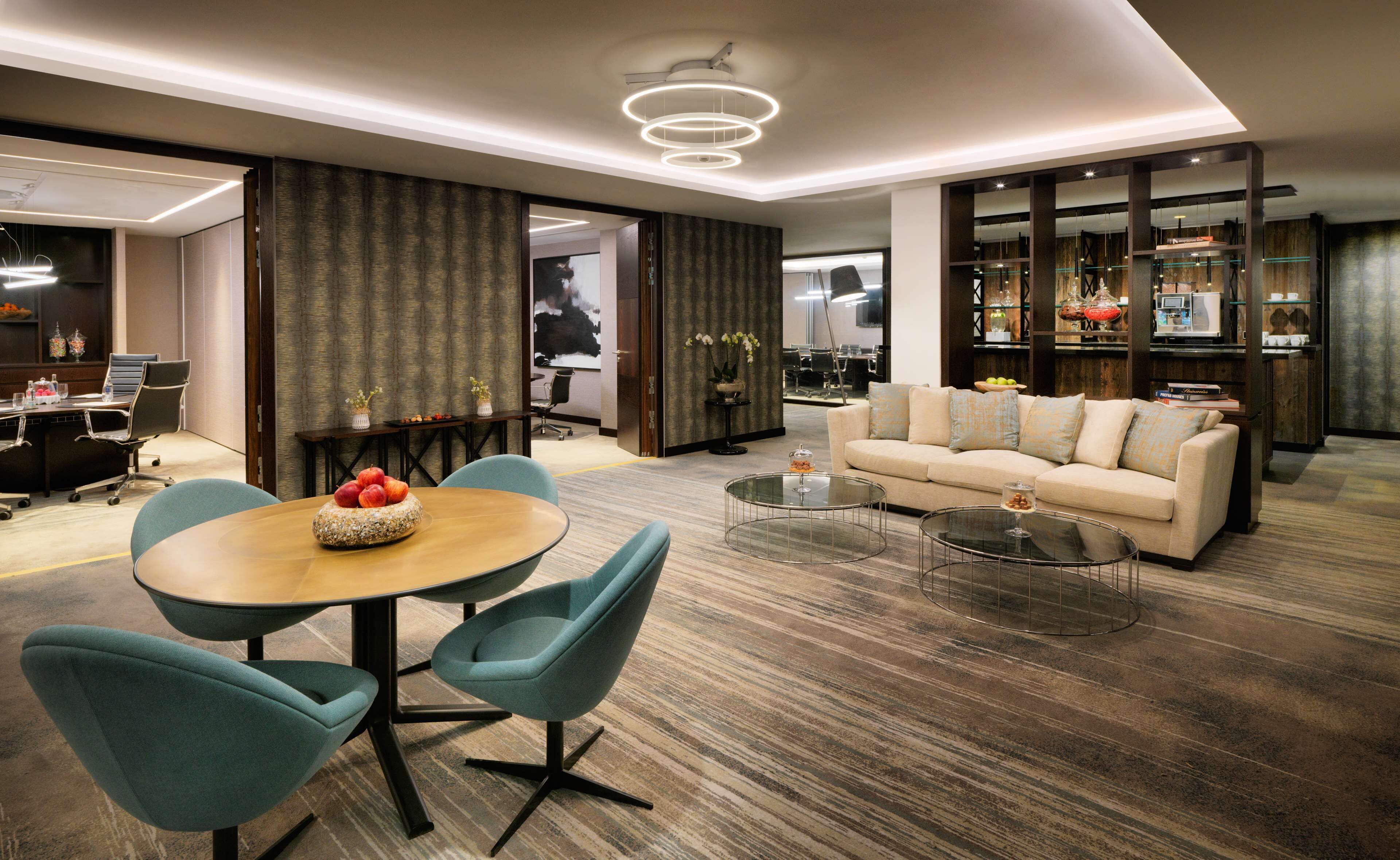A modern living room with a round dining table, teal chairs, a beige sofa, and a coffee table.