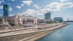 A waterfront hotel with a modern glass facade, a statue, and a riverside promenade.