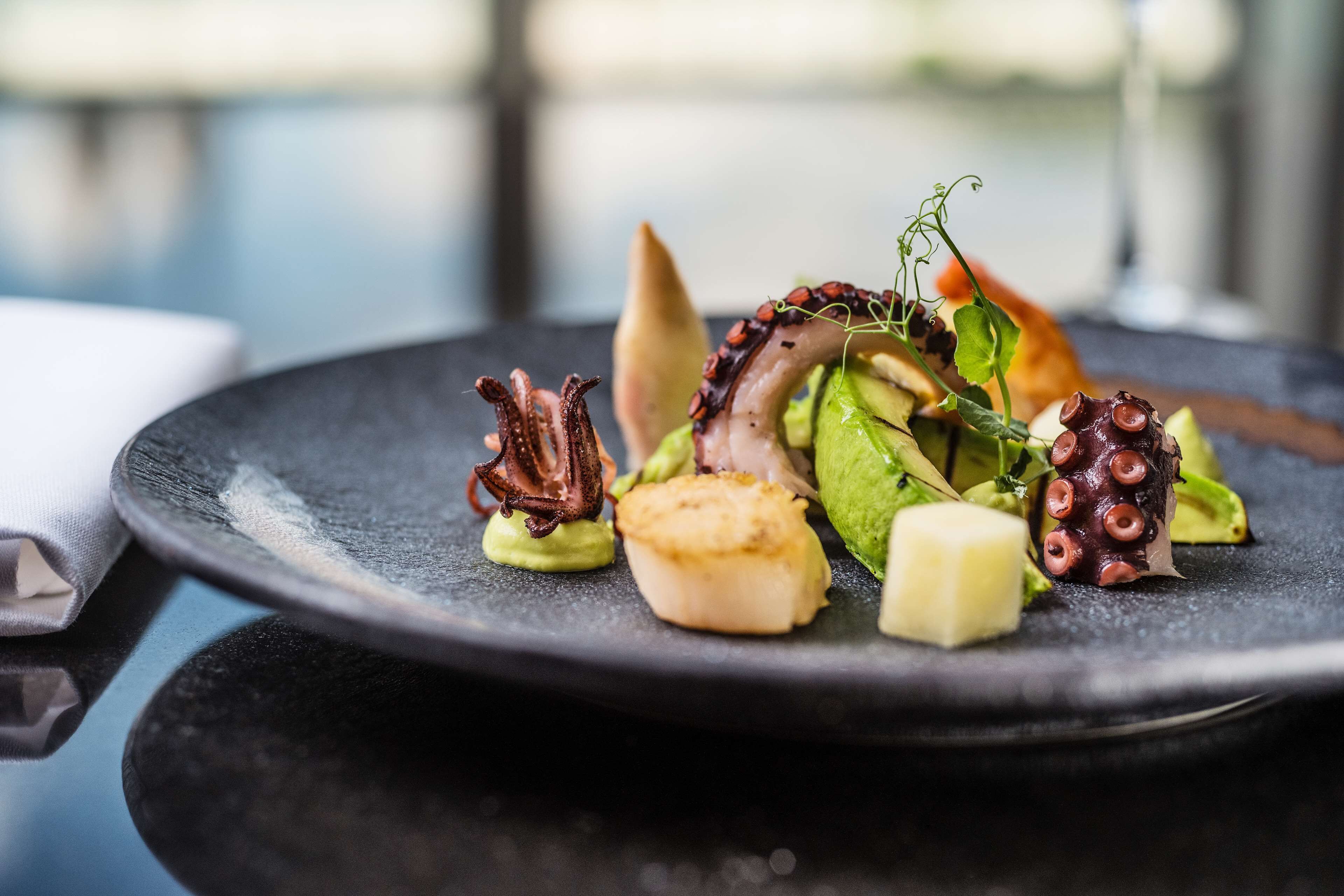A plate of food with octopus, scallops, and greens.