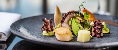 A plate of food with octopus, scallops, and greens.