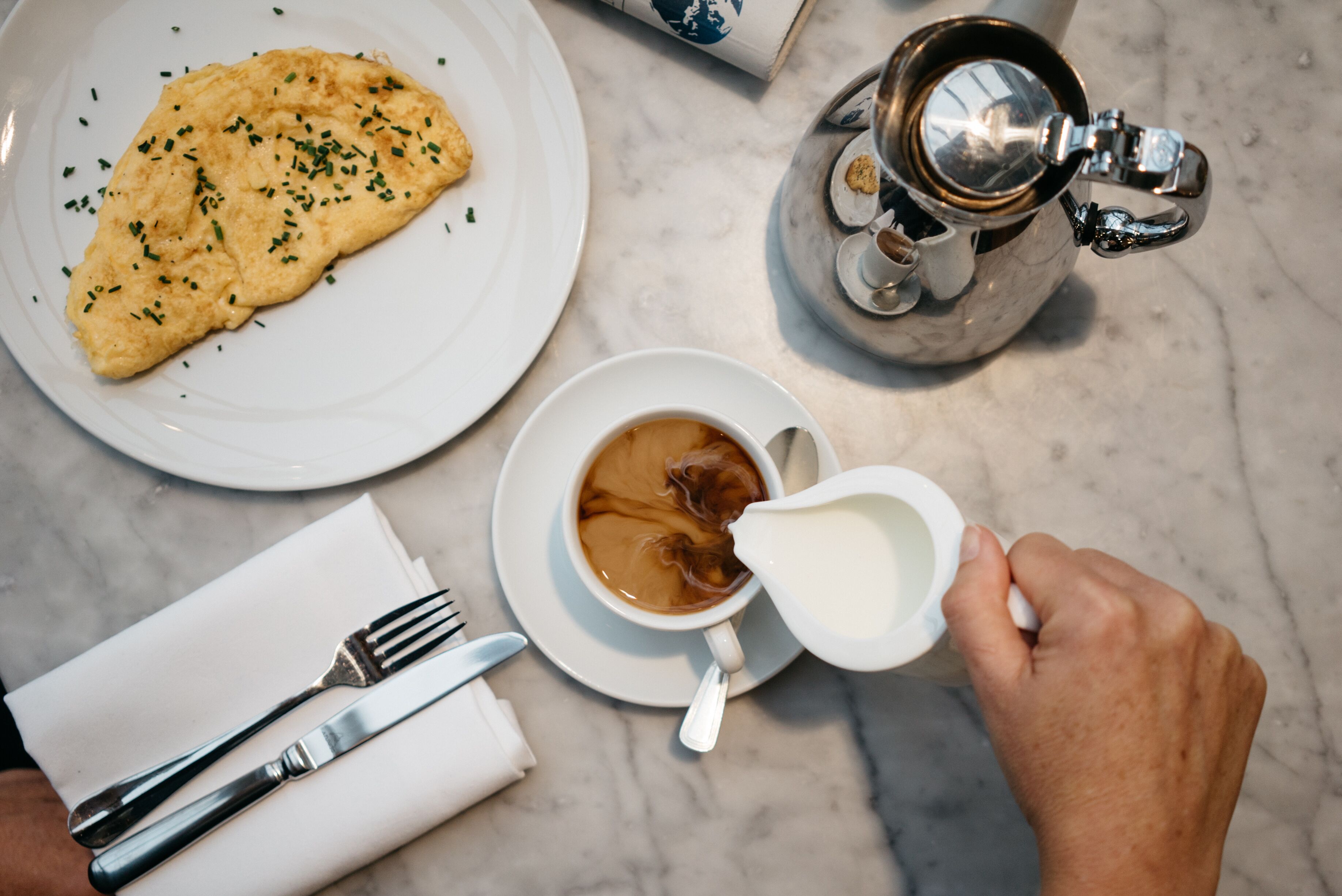 A breakfast setting with a plate of scrambled eggs, a cup of coffee, and a silver coffee pot on a marble table.