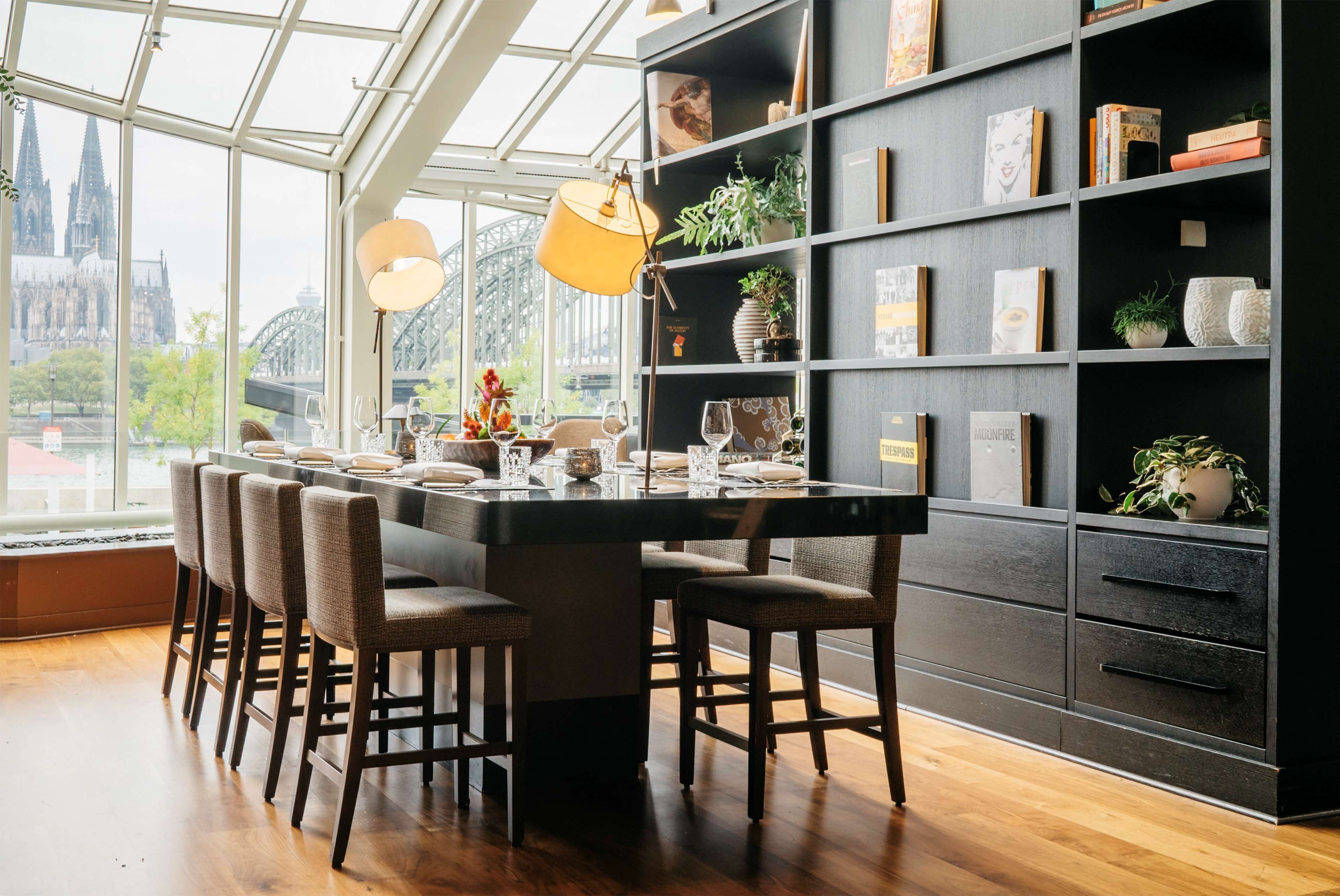 A modern dining area with a large table, chairs, and a bookshelf.