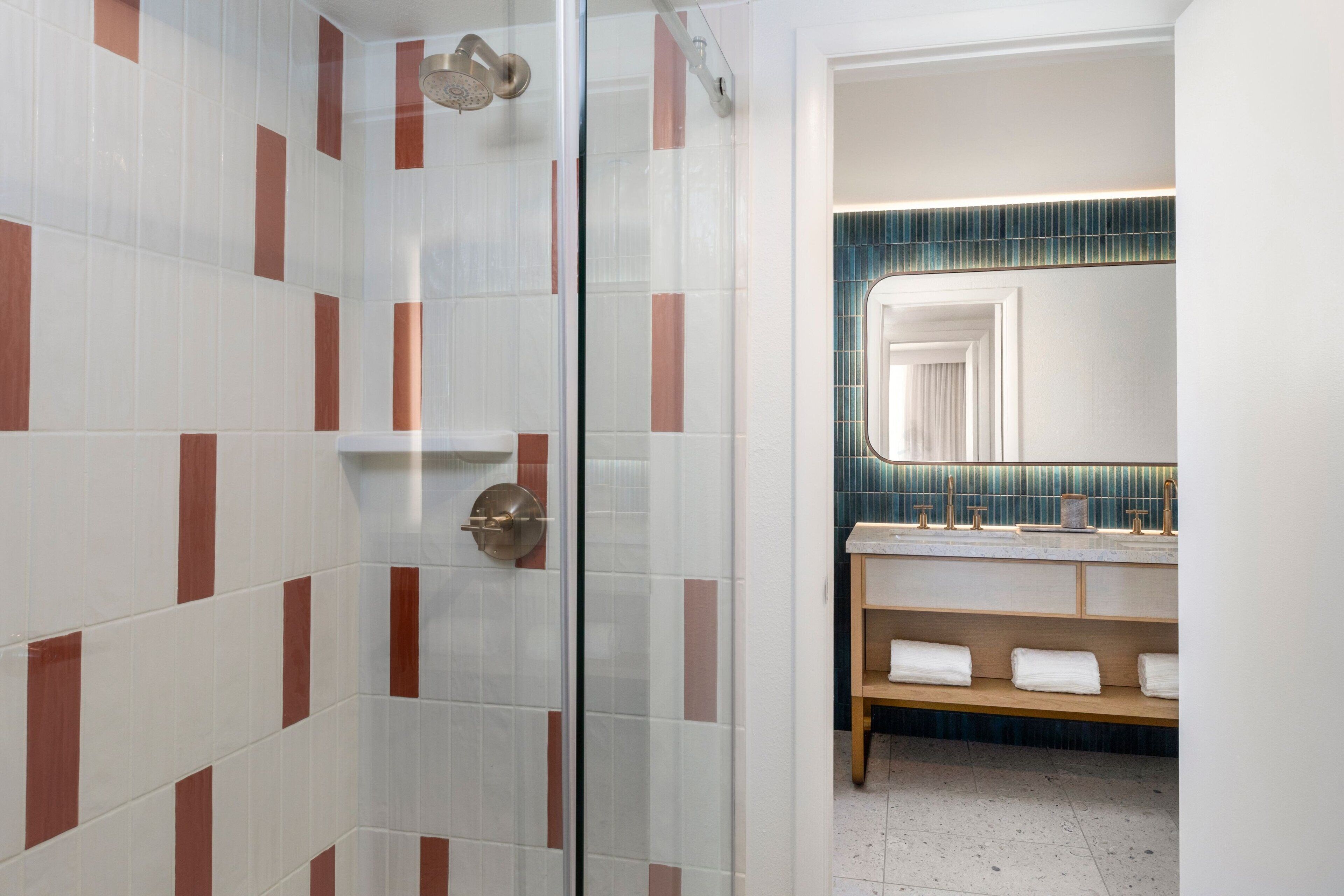 A bathroom with a glass shower door, a sink with a mirror, and a shelf with towels.
