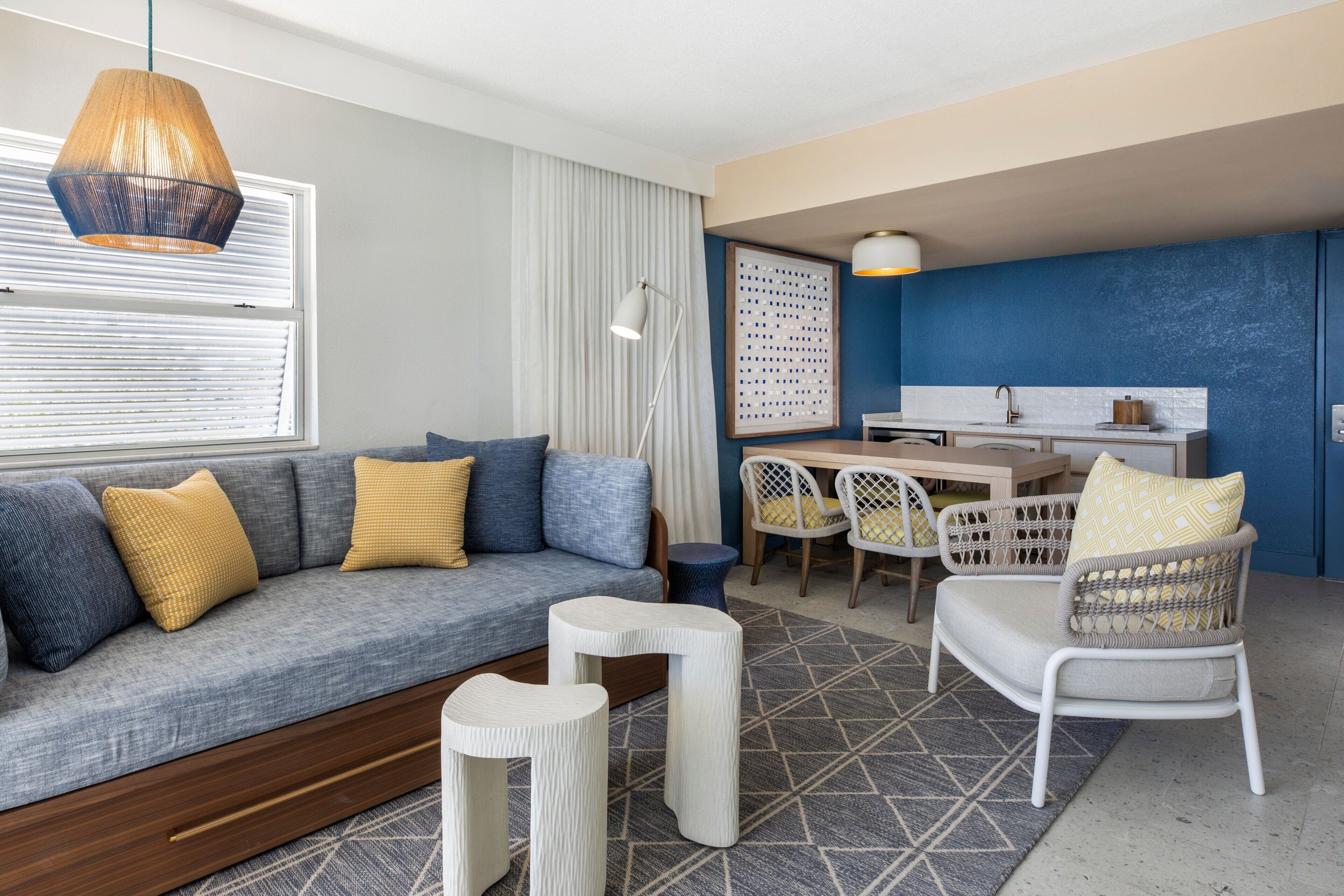 A modern living room with a sofa, armchairs, a dining table, and a kitchen area.