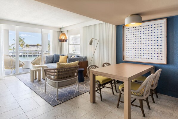 A modern living room with a large window, a dining area, and a view of the beach.