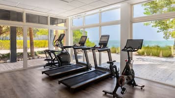 A gym with treadmills, an elliptical, and a stationary bike, large windows with a view of the sea.