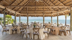 An outdoor dining area with round tables and chairs, a thatched roof, and a view of the sea. - Three Waters Resort and Marina, Islamorada, a Tribute Portfolio Resort (Islamorada)