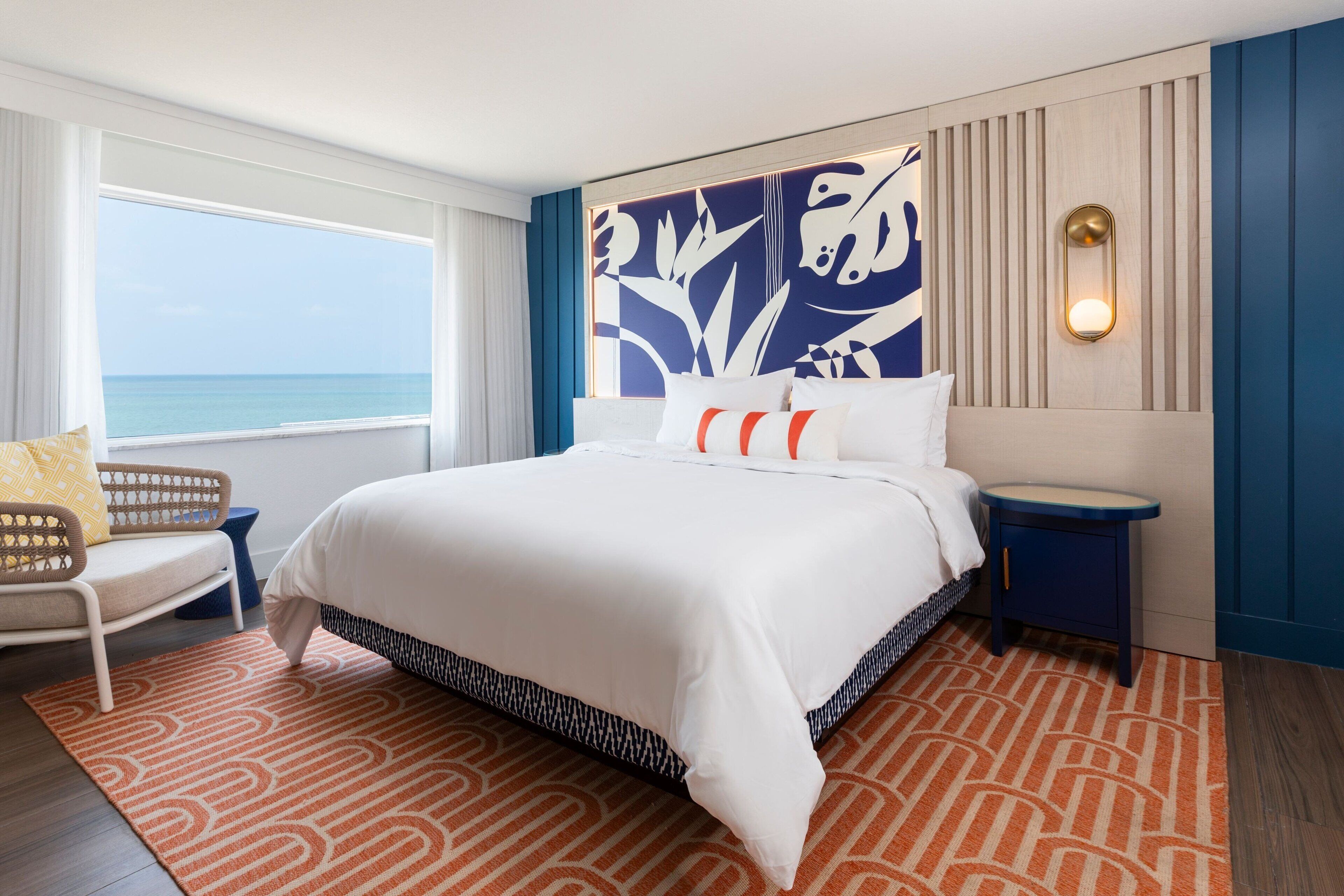 Habitación de hotel con una cama grande, vistas al mar, una silla y una mesita de noche.