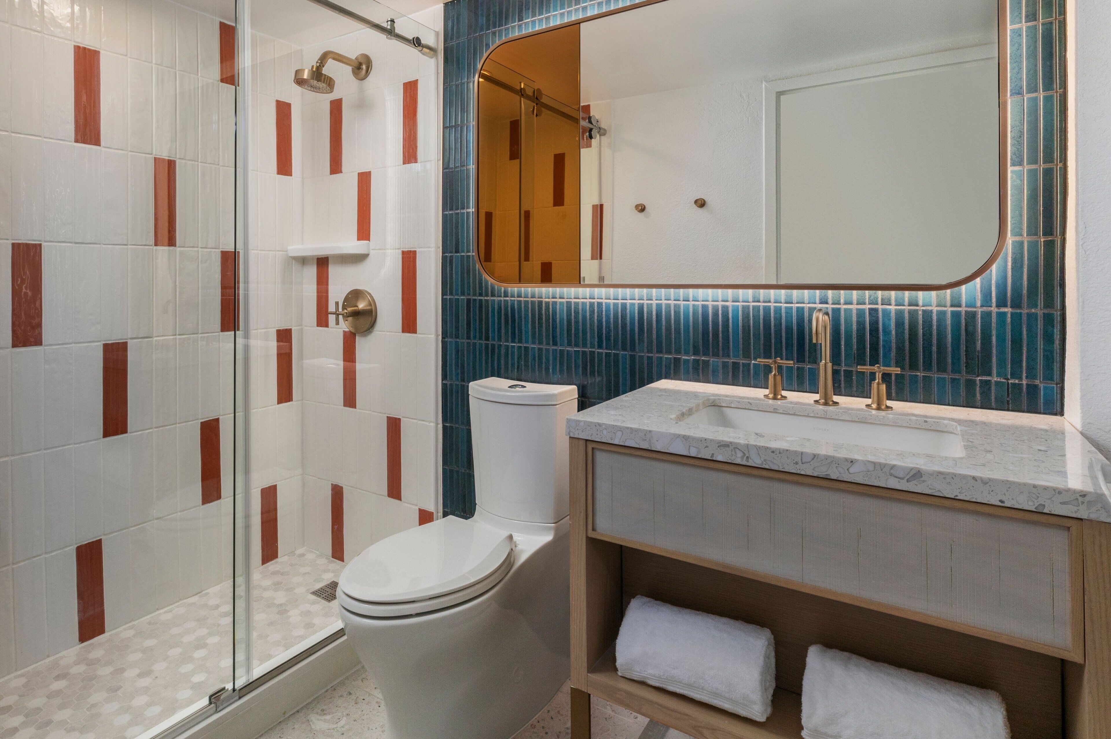 A bathroom with a glass shower enclosure, a toilet, a sink with a marble countertop, and a mirror with a wooden frame.