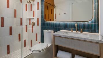A bathroom with a glass shower enclosure, a toilet, a sink with a marble countertop, and a mirror with a wooden frame.