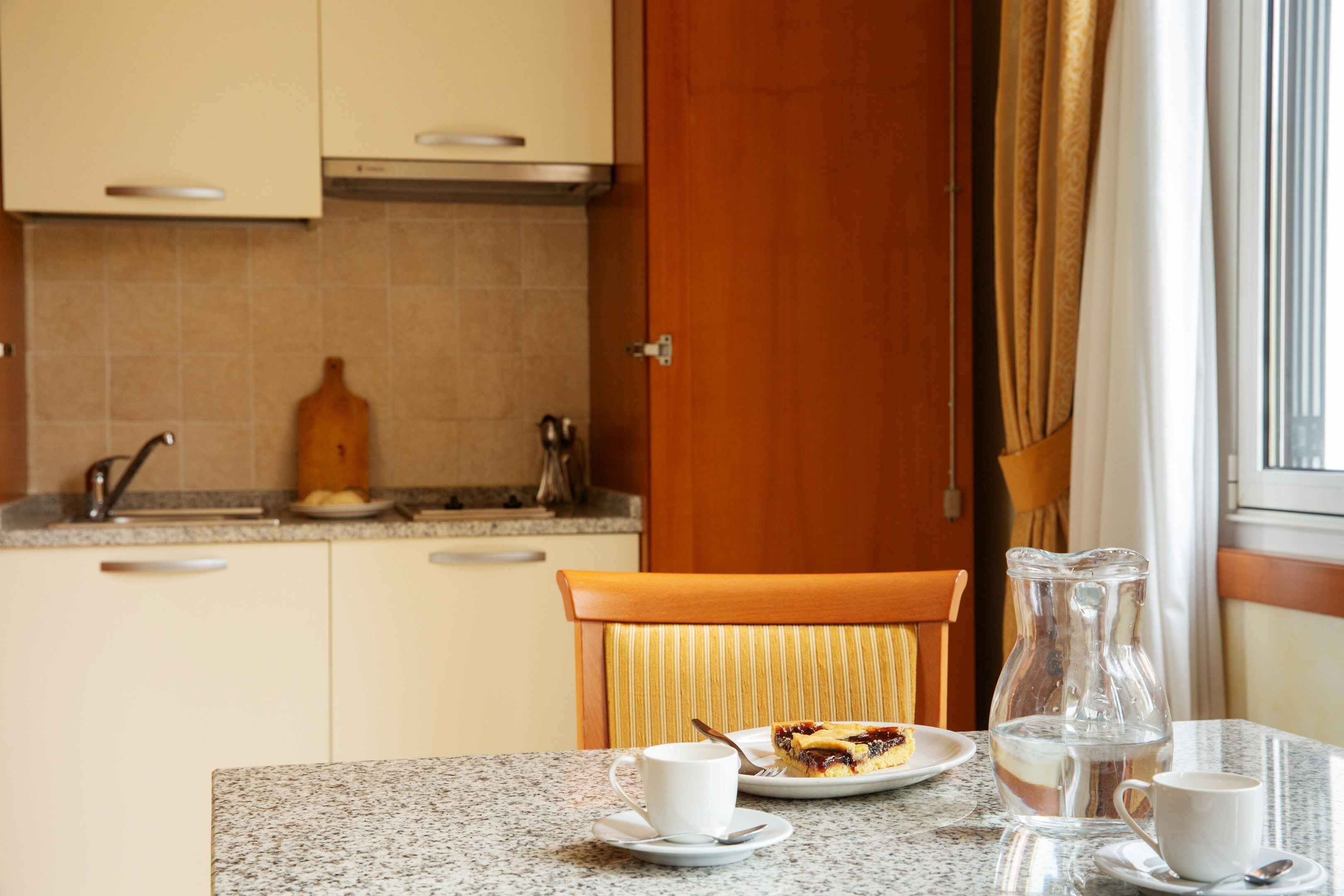 Una cocina con una mesa de comedor, sillas, una jarra y un plato con comida.