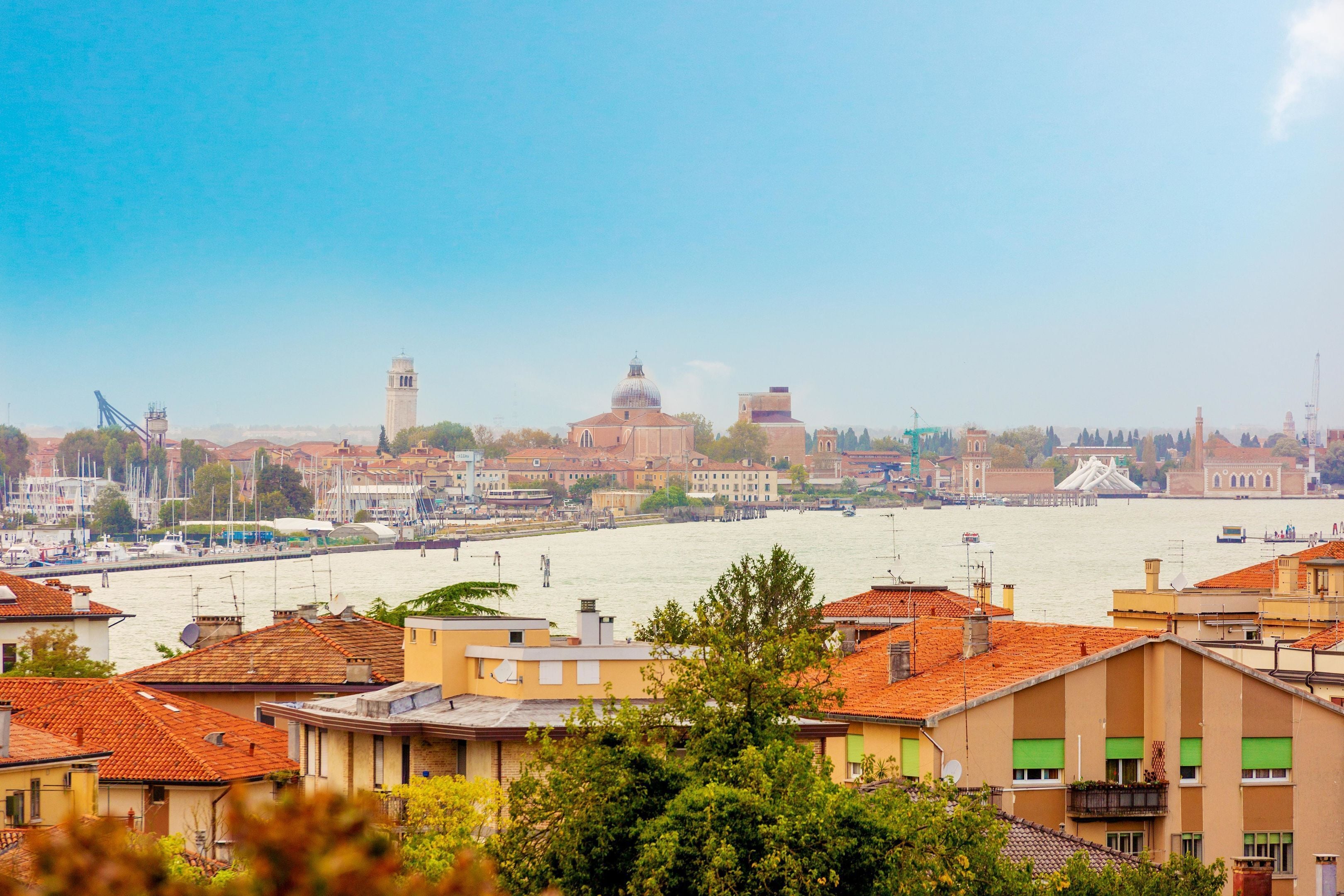 A riverfront cityscape with buildings, a tower, and boats.