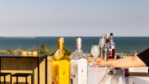 Eine Bar mit Flaschen und Gläsern, ein Holztisch und Blick auf das Meer.
