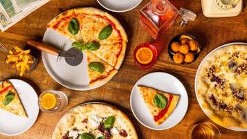 Ein Holztisch mit verschiedenen Pizzen, einem Pizzaroller, einem Glas Orangensaft, einem Glas Bier und einem Salzstreuer.