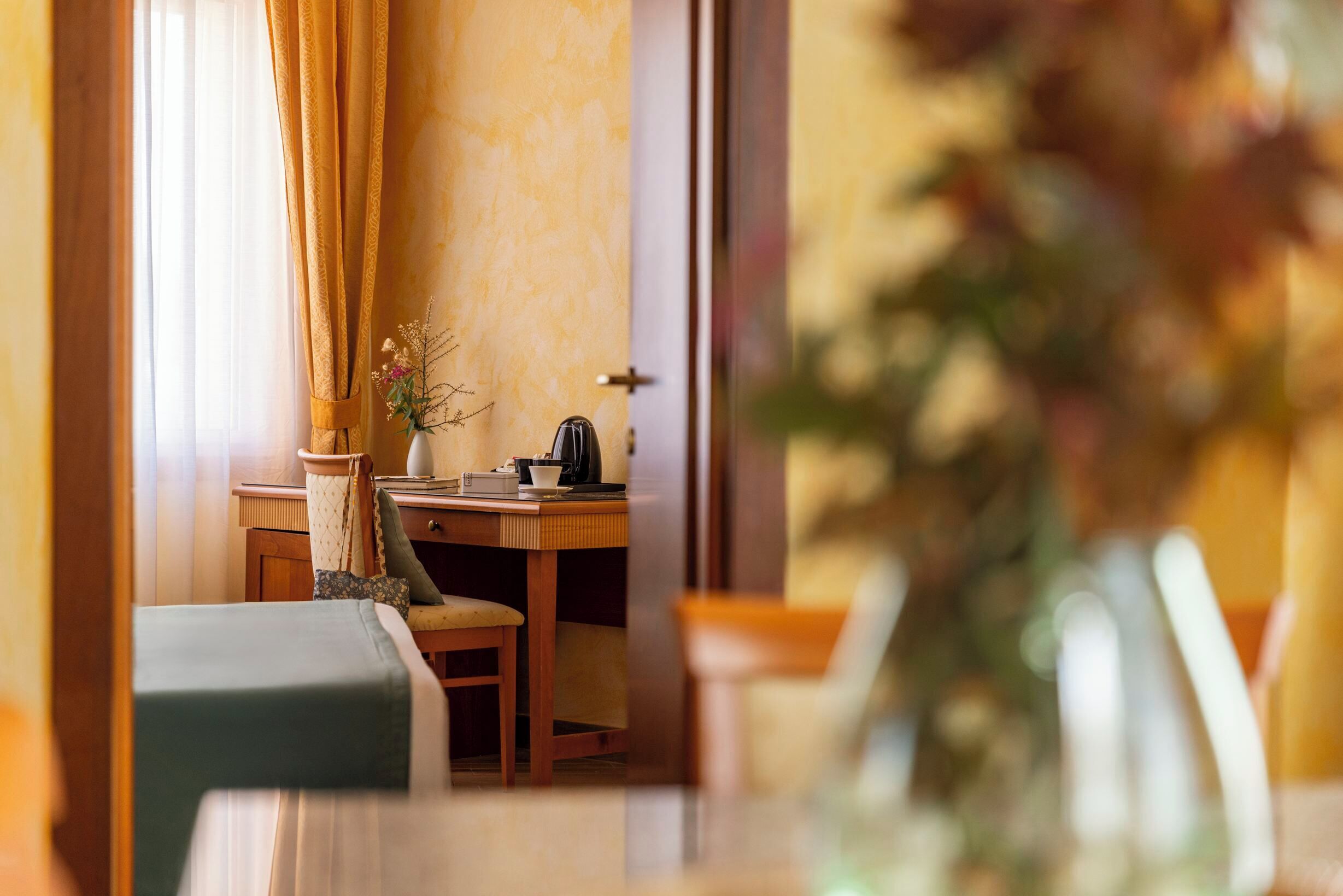 A cozy room with a wooden desk, a chair, a small table, and a vase with flowers.
