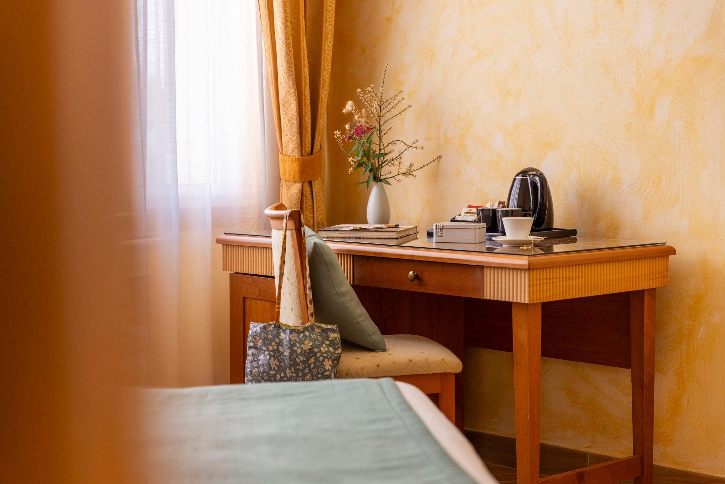 Ein Hotelzimmer mit einem Holztisch, einem Stuhl, einem Bett, einer Vase mit Blumen und einer Kaffeemaschine.