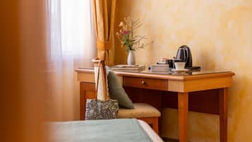Ein Hotelzimmer mit einem Holztisch, einem Stuhl, einem Bett, einer Vase mit Blumen und einer Kaffeemaschine.