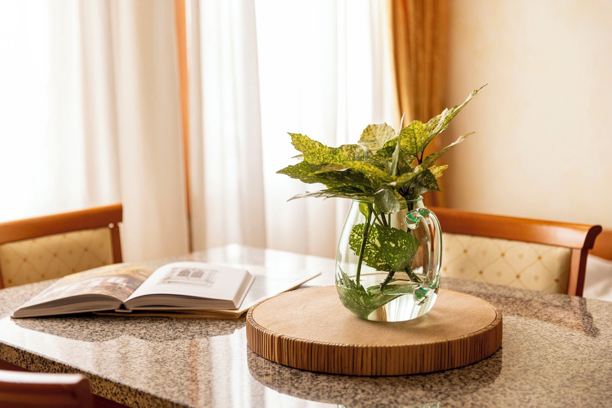 A clear glass vase with green leaves on a wooden coaster on a granite table.