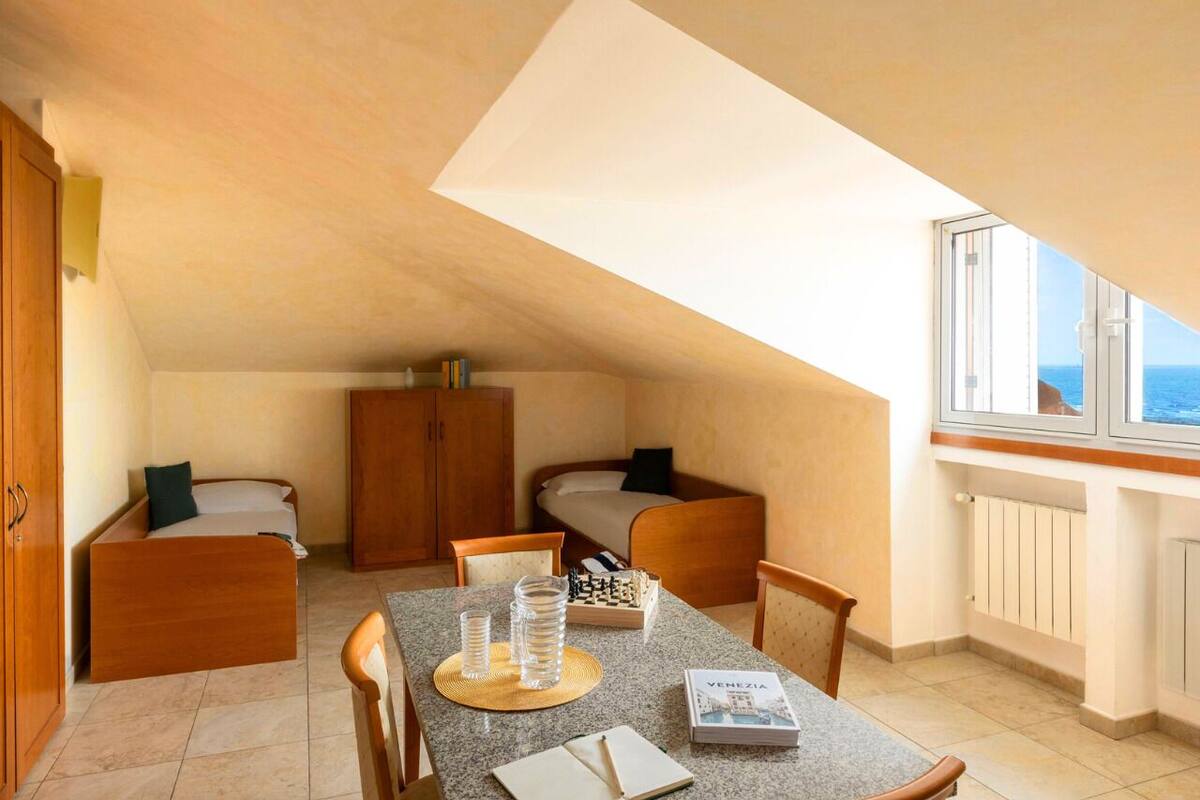A compact room with a dining table, two beds, and a window with a view.