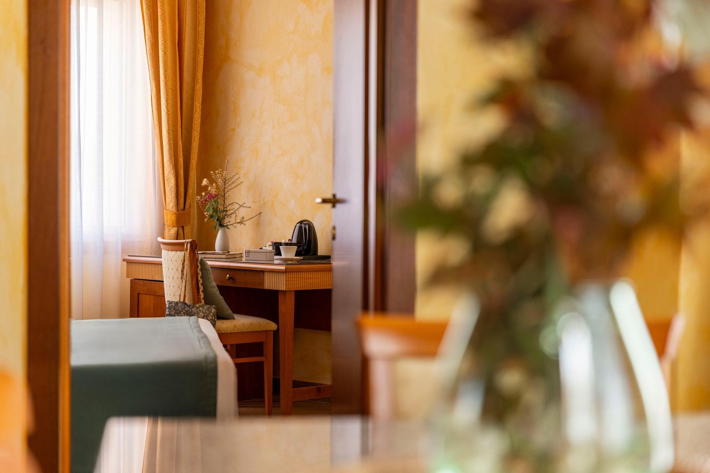 A room with a desk, chair, and a vase with flowers.