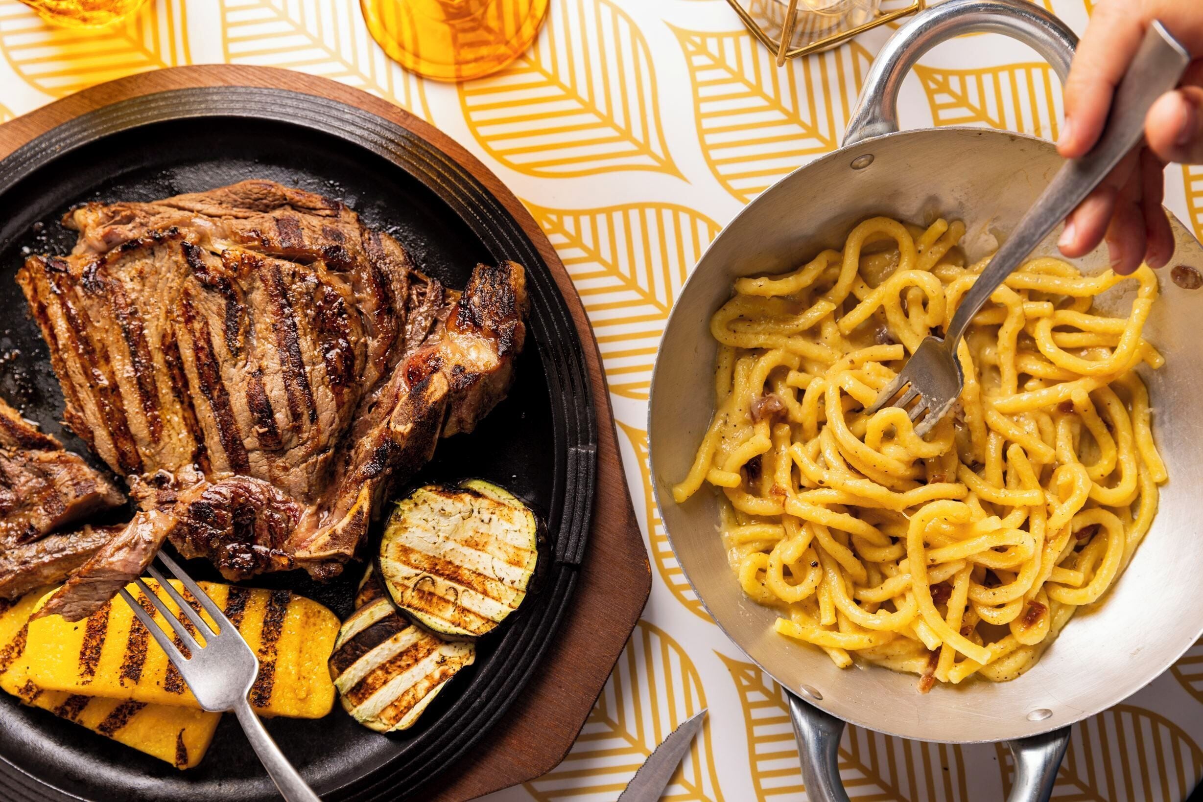 Une assiette avec un steak grillé et des légumes grillés, et une poêle contenant des pâtes.