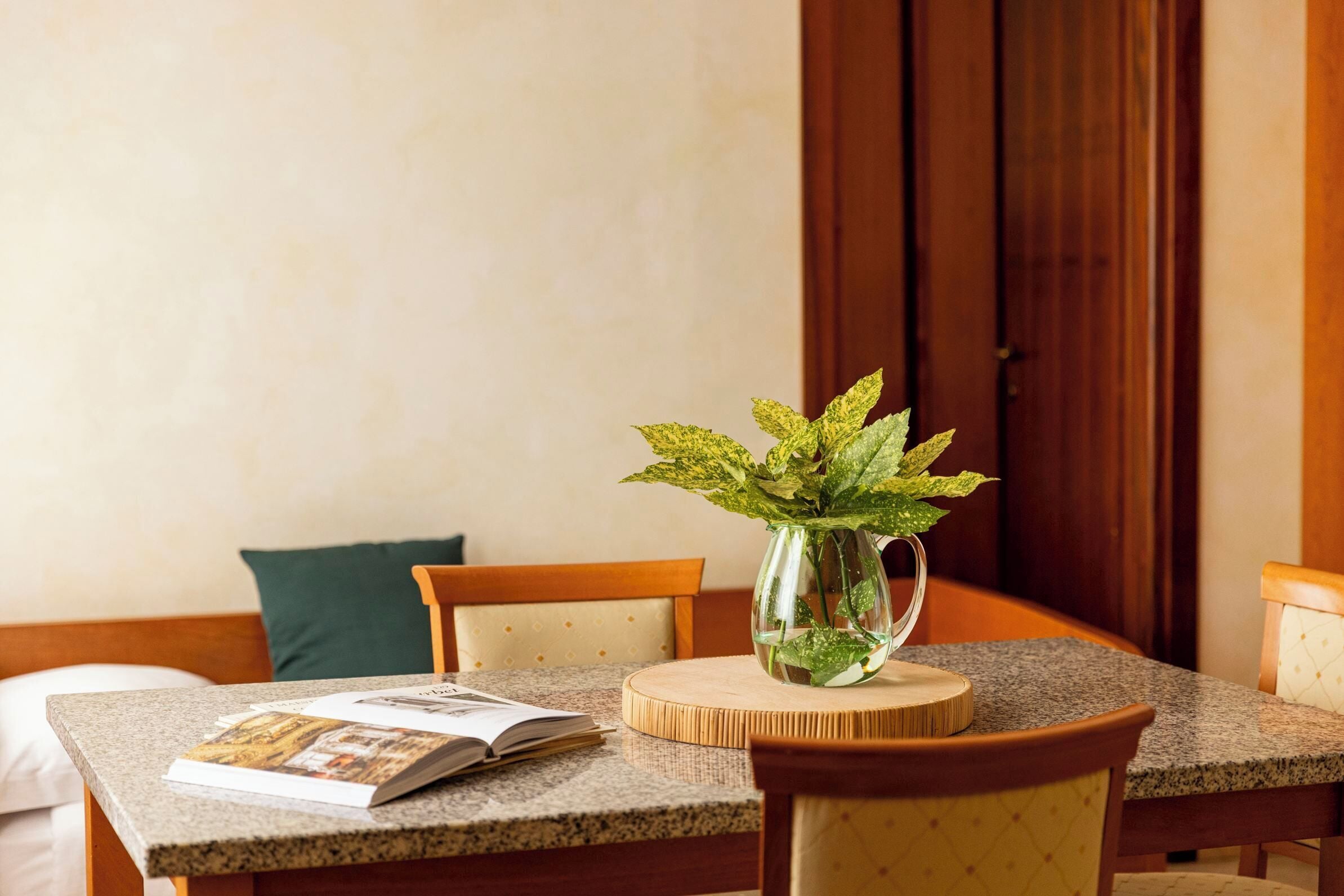 A dining area with a table, chairs, a book, and a glass vase with a plant.
