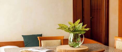 A dining area with a table, chairs, a book, and a glass vase with a plant.