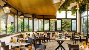 Ein Restaurant mit Außenbereich, Tischen mit gelasstem Glas und hängenden Pflanzen.