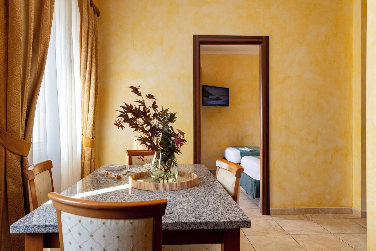 A dining area with a granite table, chairs, a vase with flowers, and a painting on the wall.