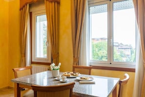 A dining area with a table, chairs, a window with curtains, and a view of greenery outside. - Hotel Residence Venezia 2000 (Venice)