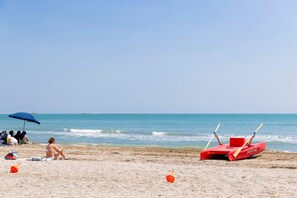 A beach with a lifeguard stand, a woman sitting on the sand, and a blue umbrella. - Hotel Residence Venezia 2000 (Venice)
