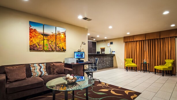 A hotel lobby with a reception desk, a sofa, two yellow chairs, a glass coffee table, and a large autumn-themed painting on the wall. - Best Western Heritage Inn (Vacaville)