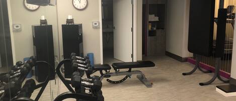 A gym with exercise equipment, a clock, and a door leading to a bathroom.