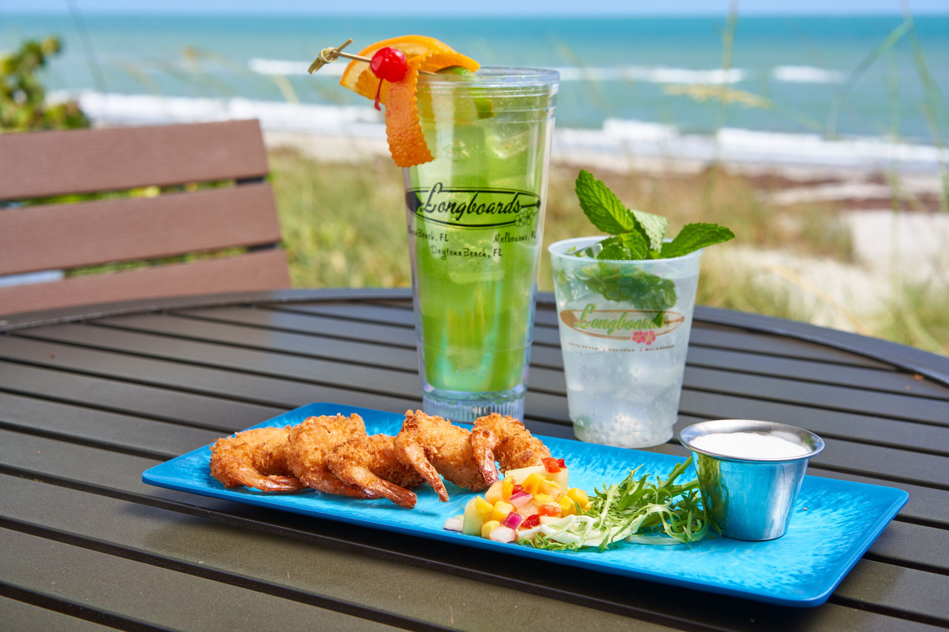 Un tavolo con un piatto blu di gamberi fritti, un bicchiere di cocktail verde e una bevanda alla menta.