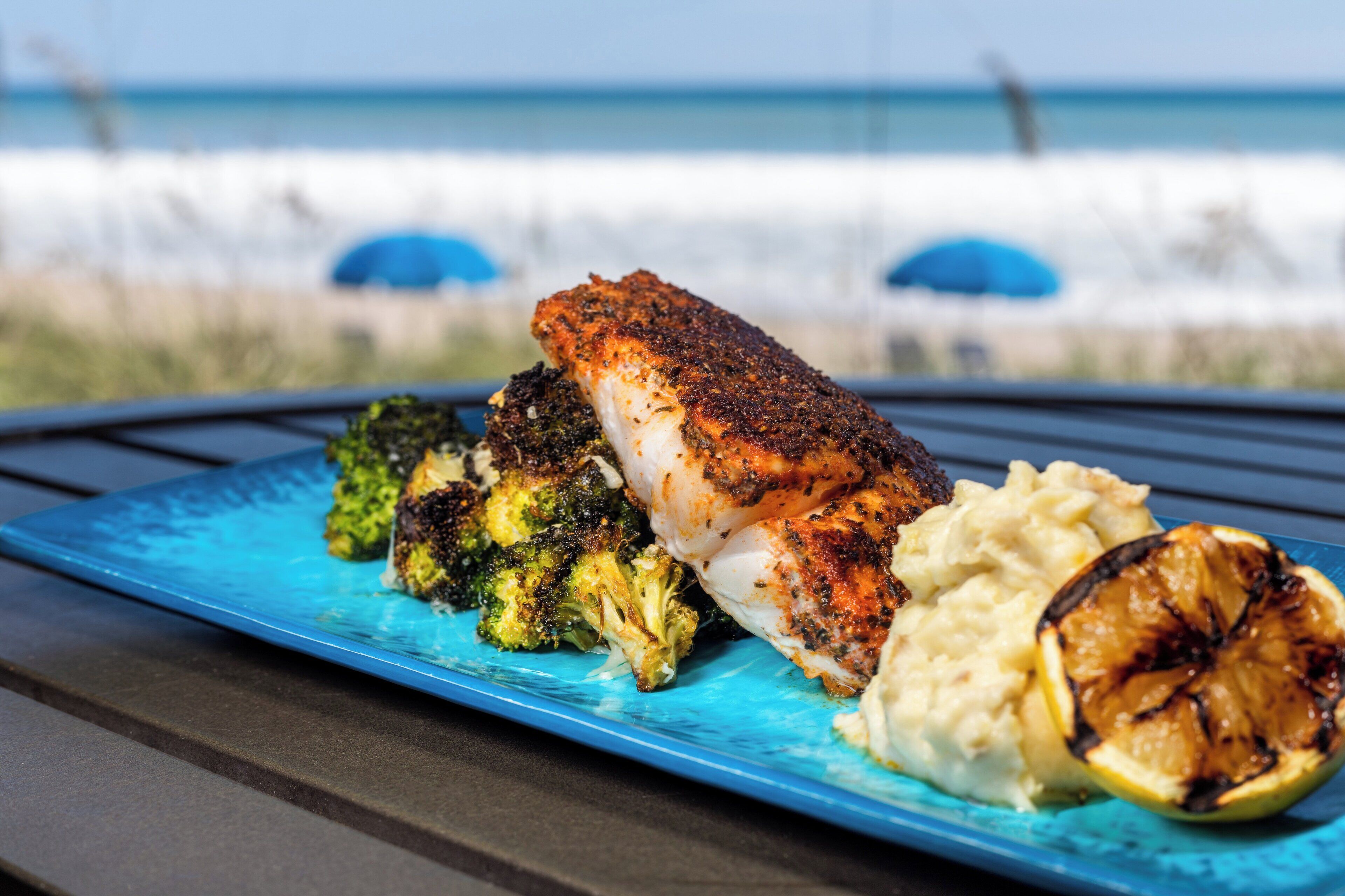 A meal with fish, broccoli, and lemon on a blue plate.