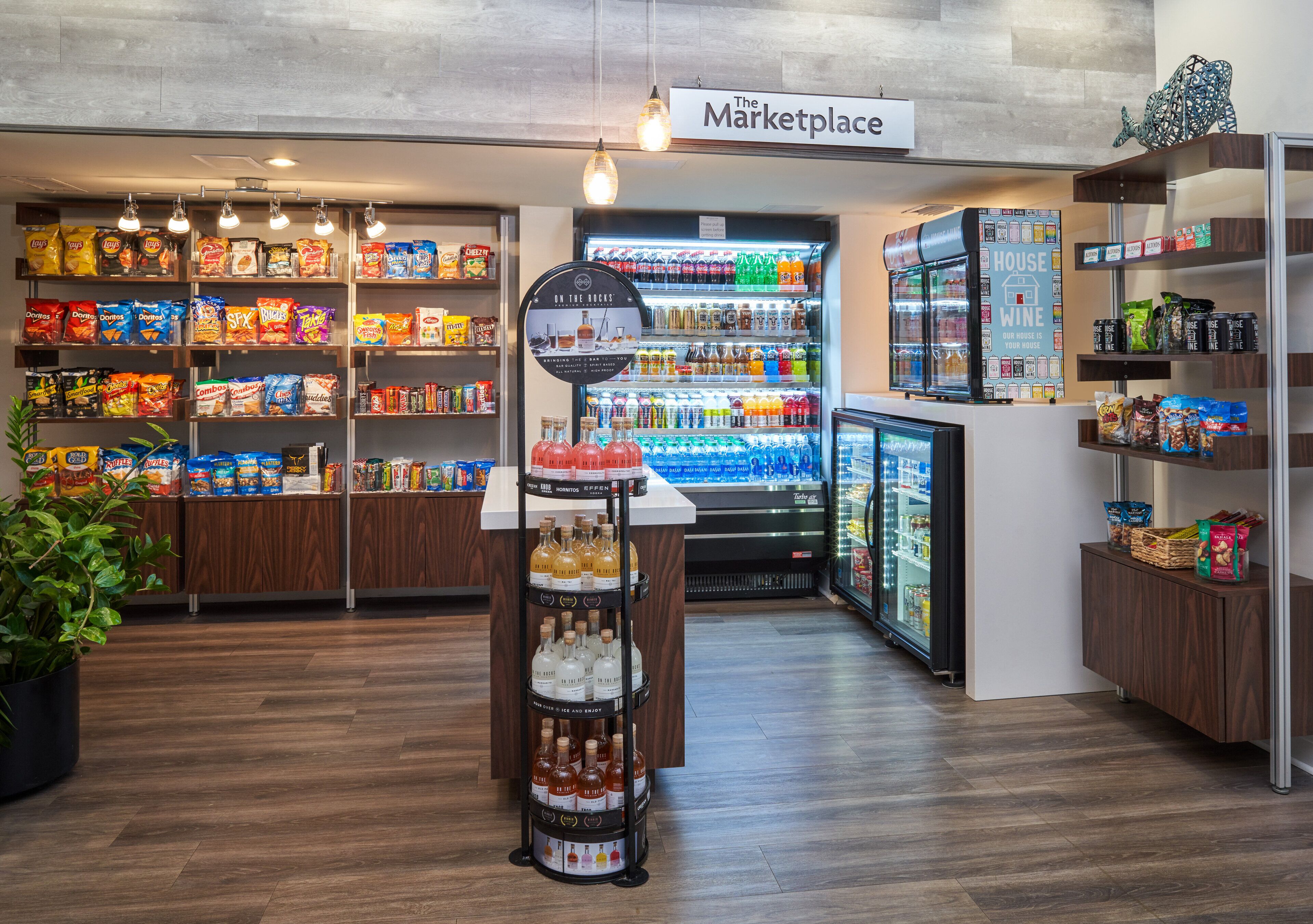 Interno di un negozio di alimentari con scaffali pieni di snack, un reparto refrigerato e una selezione di vini.
