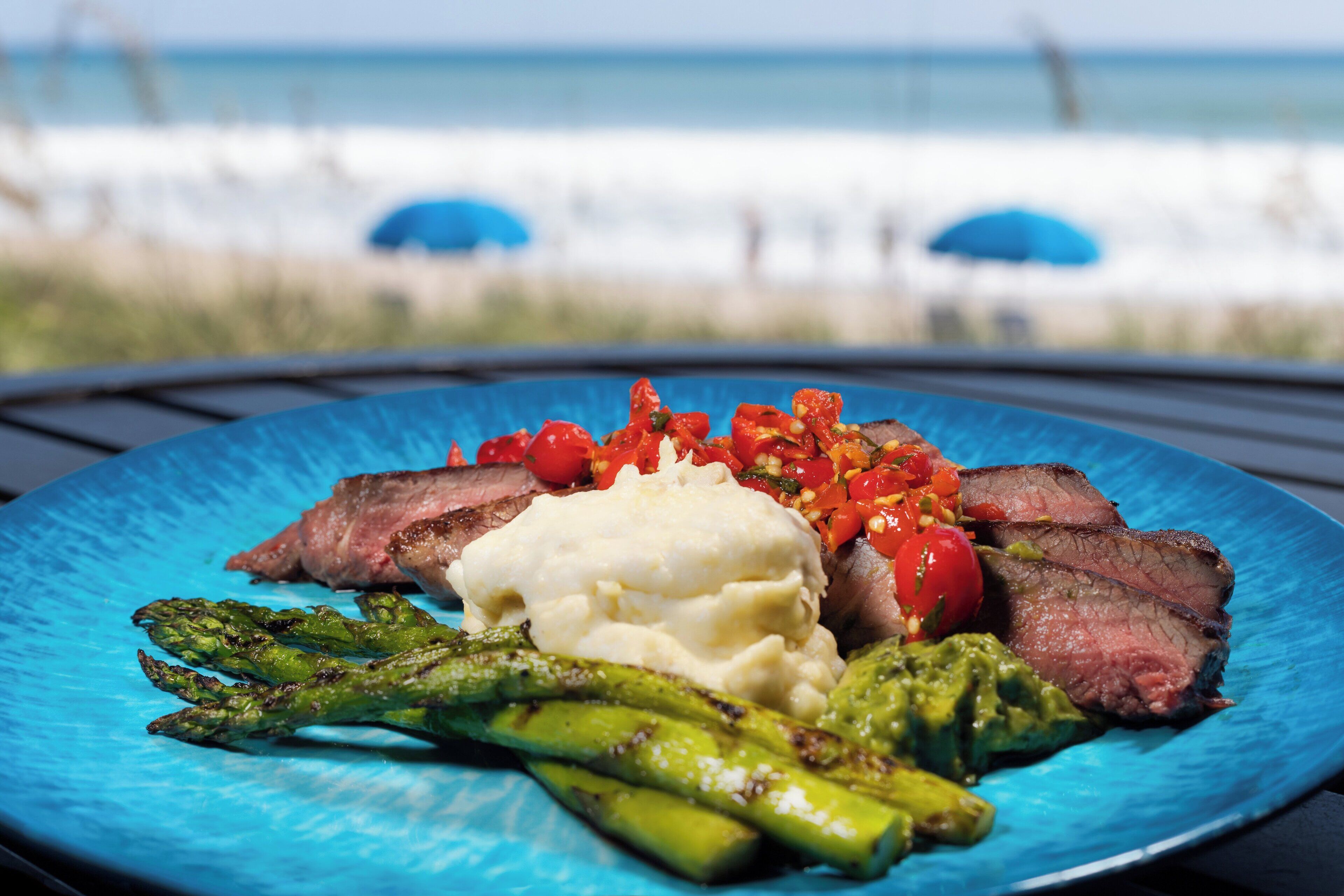 A blue plate with steak, asparagus, mashed potatoes, and a tomato-based sauce.