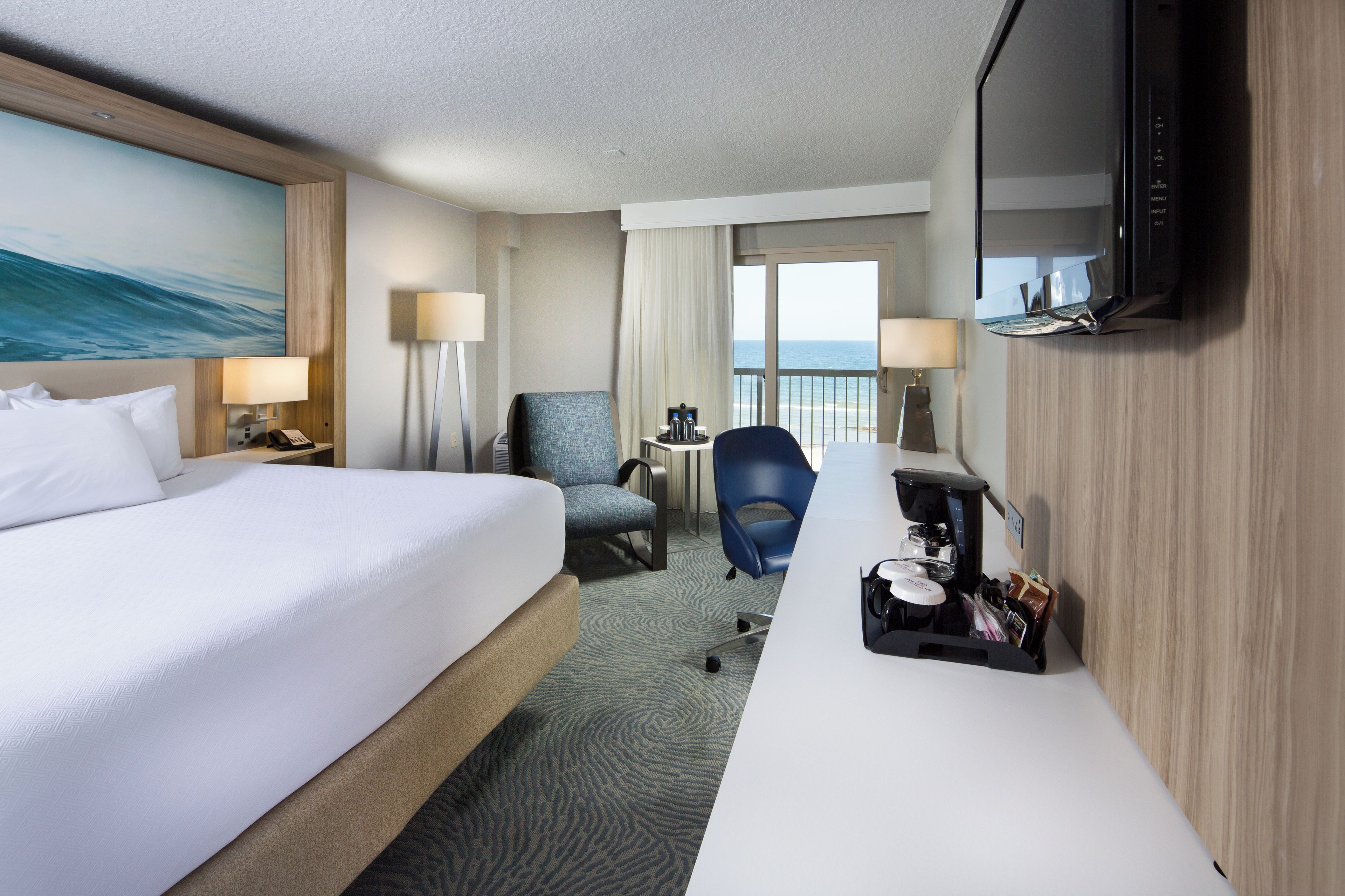 Habitación de hotel con cama, escritorio, silla, televisor y vista al mar.