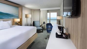Habitación de hotel con cama, escritorio, silla, televisor y vista al mar.