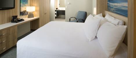 A hotel room with a large bed, a desk with a lamp, a chair, and a television.