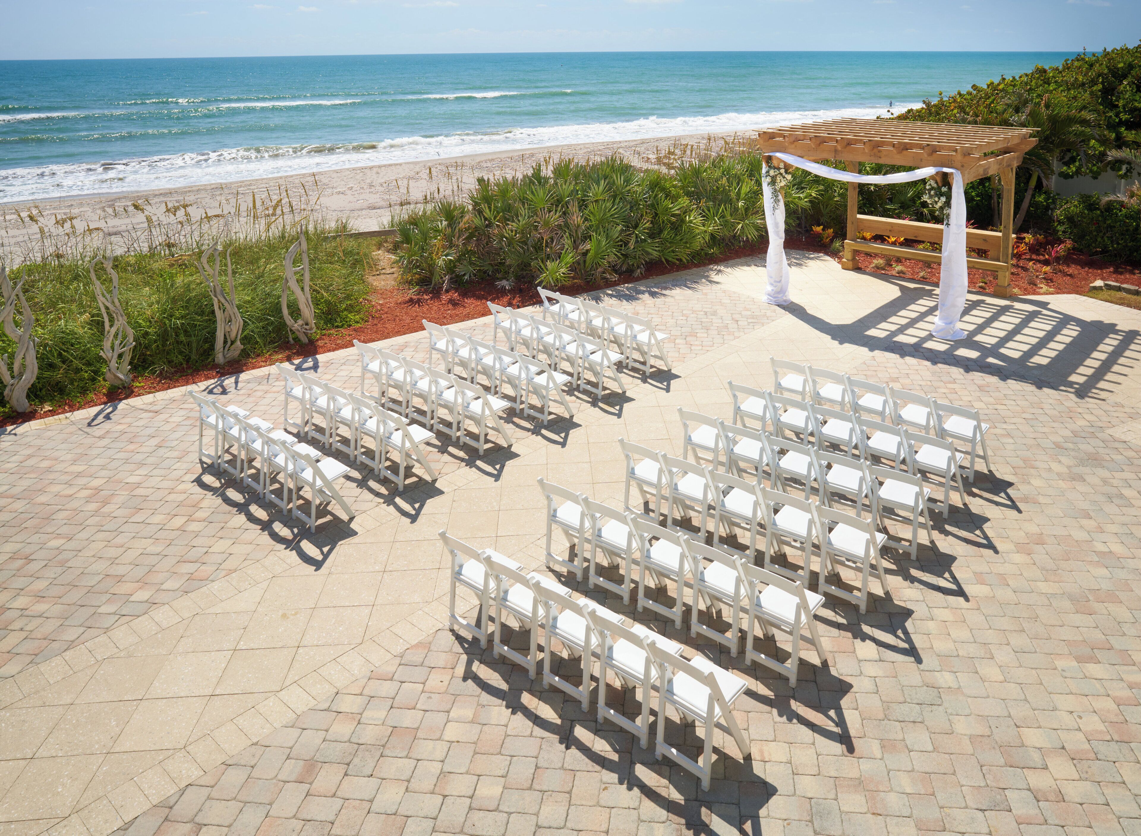 Une cérémonie de mariage en plein air, avec des chaises blanches et une arche en bois donnant sur la plage.