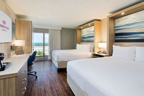 A hotel room with two beds, a desk with a lamp, a chair, and a view of the ocean. - Crowne Plaza Melbourne - Oceanfront by IHG (Indialantic)
