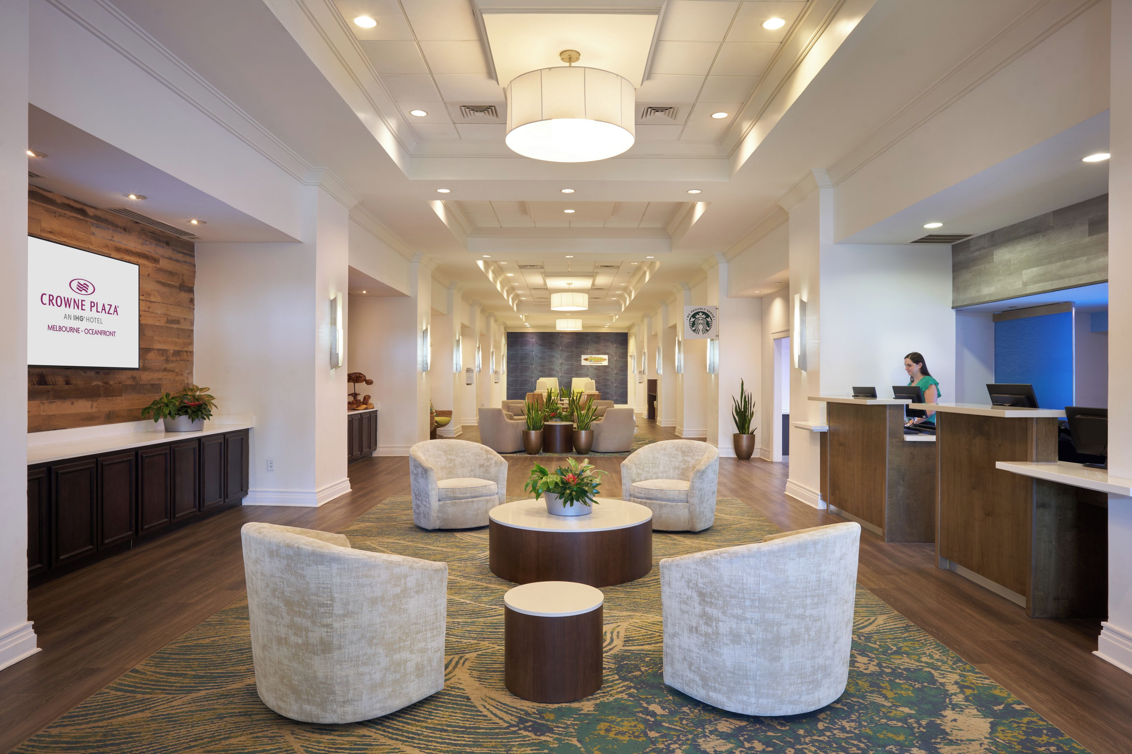 A hotel lobby with a reception desk, seating area, and a large screen displaying the hotel name.