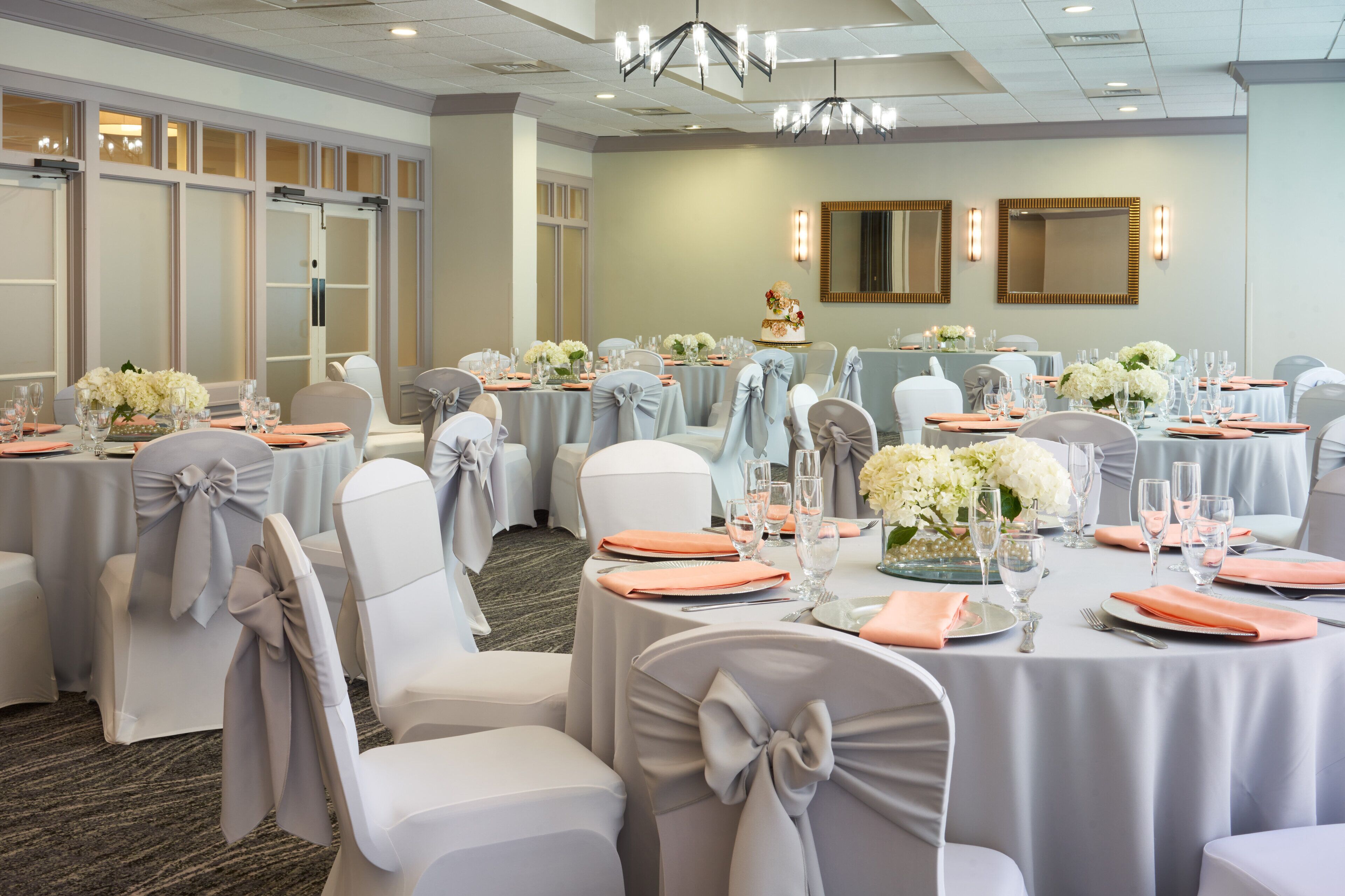 A banquet hall with round tables, chairs with bows, and floral centerpieces.