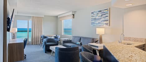 A hotel room with a balcony, a sofa, a desk, and a kitchenette.