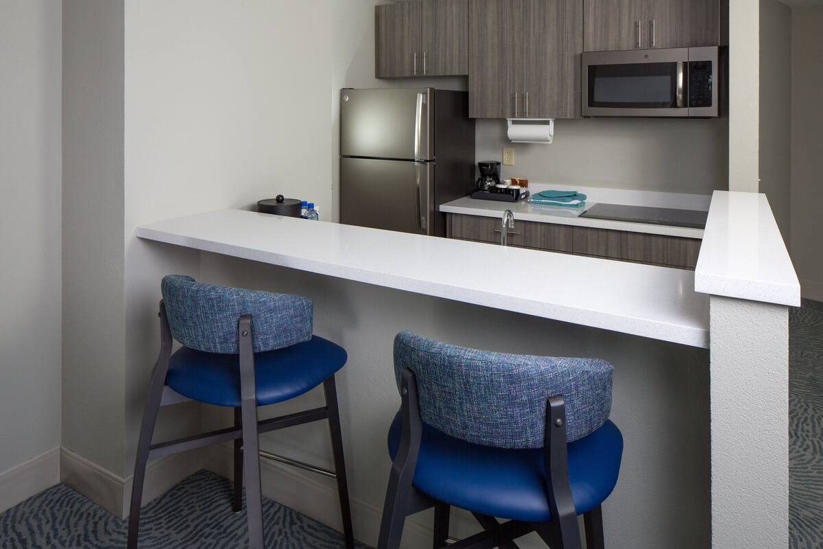 A compact kitchen with a refrigerator, microwave, and bar stools.