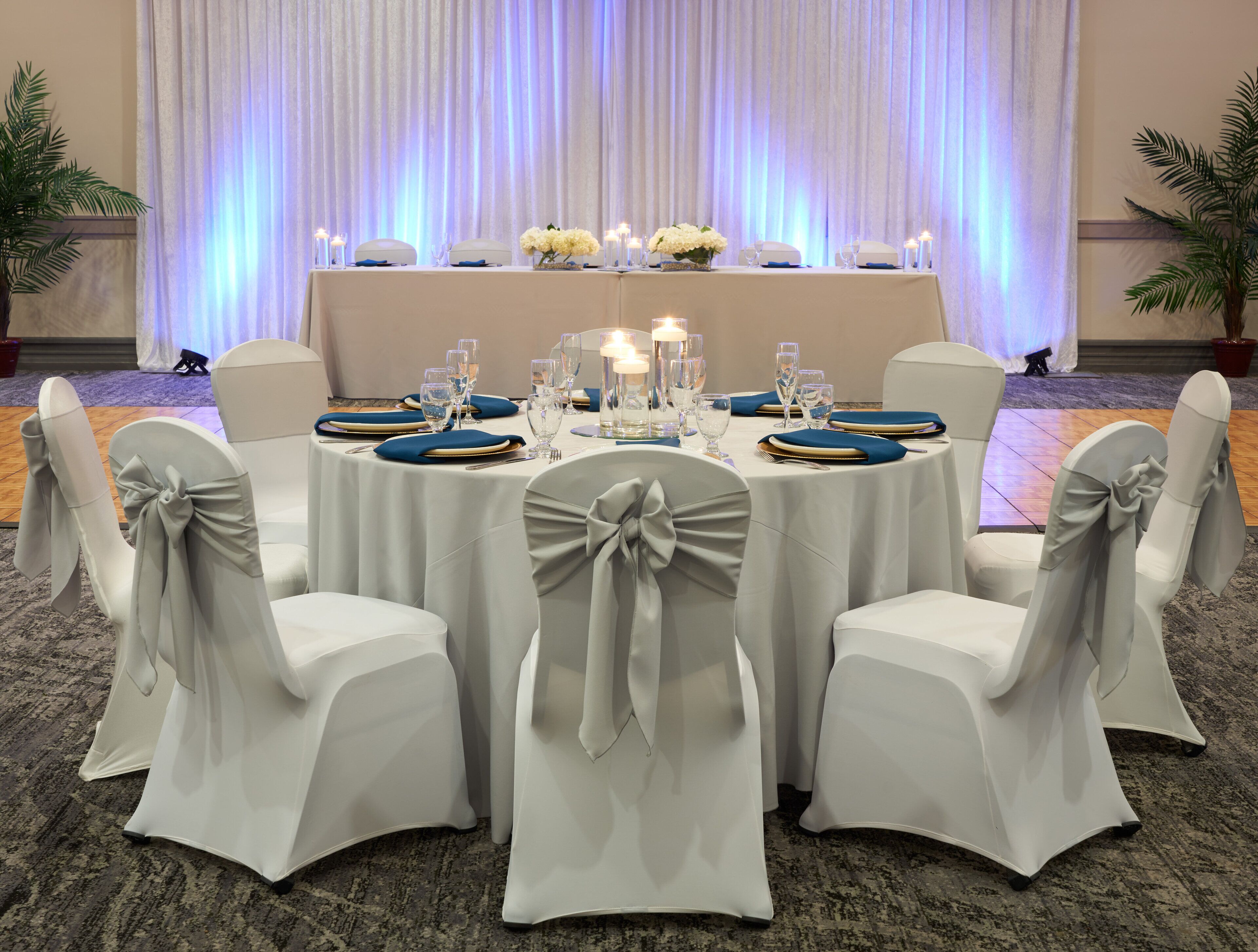 A round table with white chairs, each with a bow on the backrest, set for a formal event.
